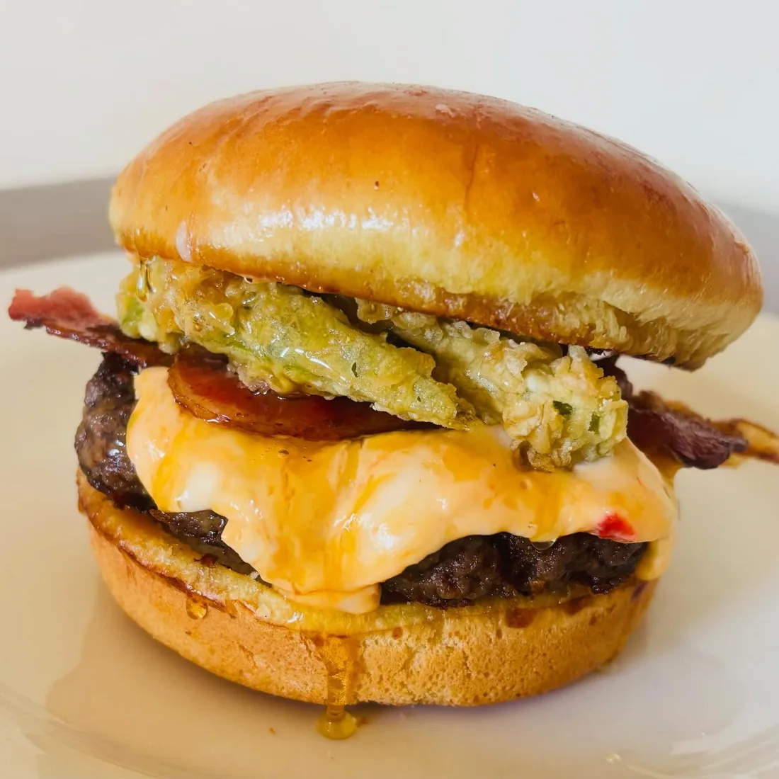 A burger stacked with fried green tomato, melted cheese and bacon