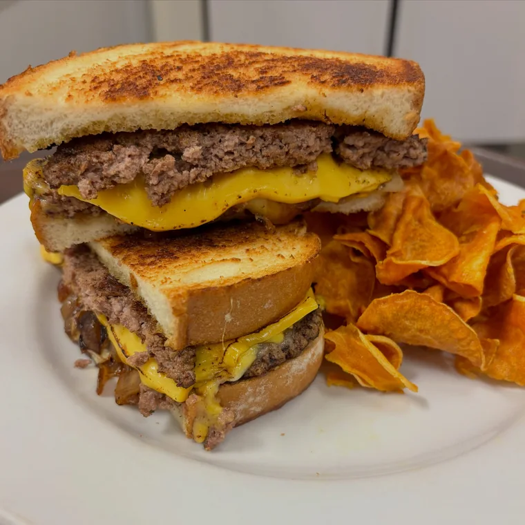 A patty melt on toasted bread with house chips